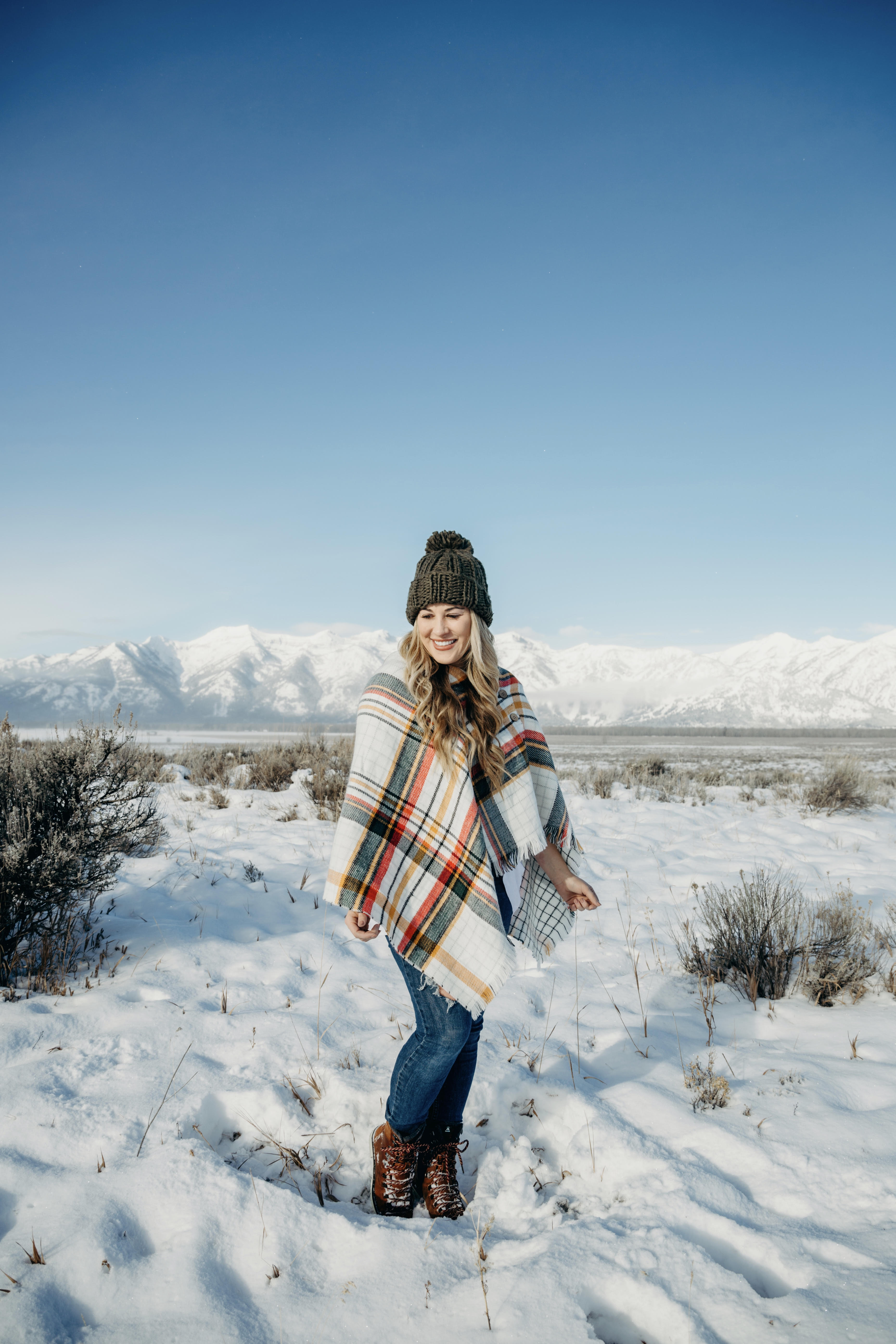 Cold Weather essentials featured by top US fashion blog, Walking in Memphis in High Heels: image of a woman wearing aGrace & Lace plaid poncho, Free People skinny jeans, Grace & Lace pom beanie, and KAMIK hiking boots