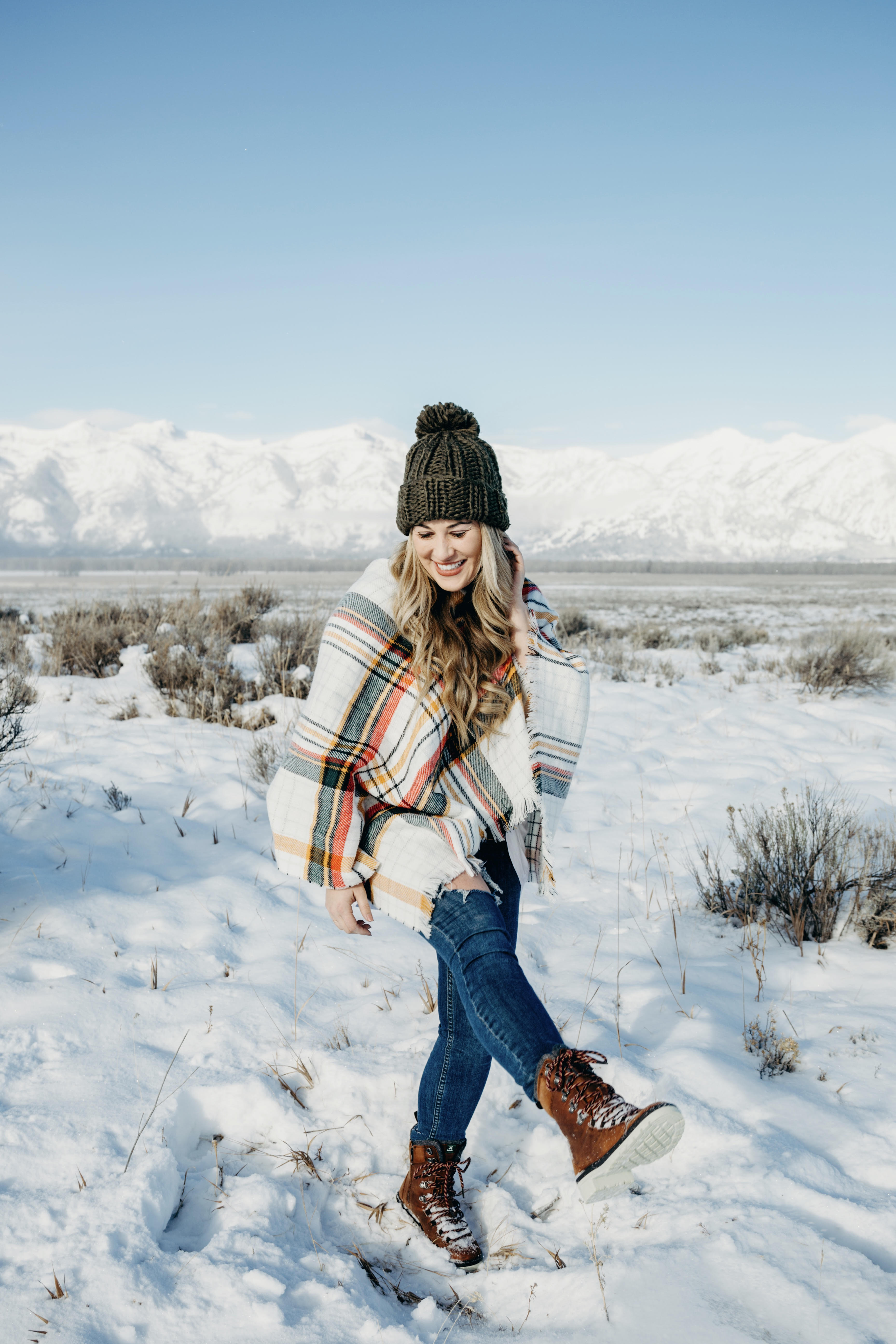 Cold Weather essentials featured by top US fashion blog, Walking in Memphis in High Heels: image of a woman wearing aGrace & Lace plaid poncho, Free People skinny jeans, Grace & Lace pom beanie, and KAMIK hiking boots