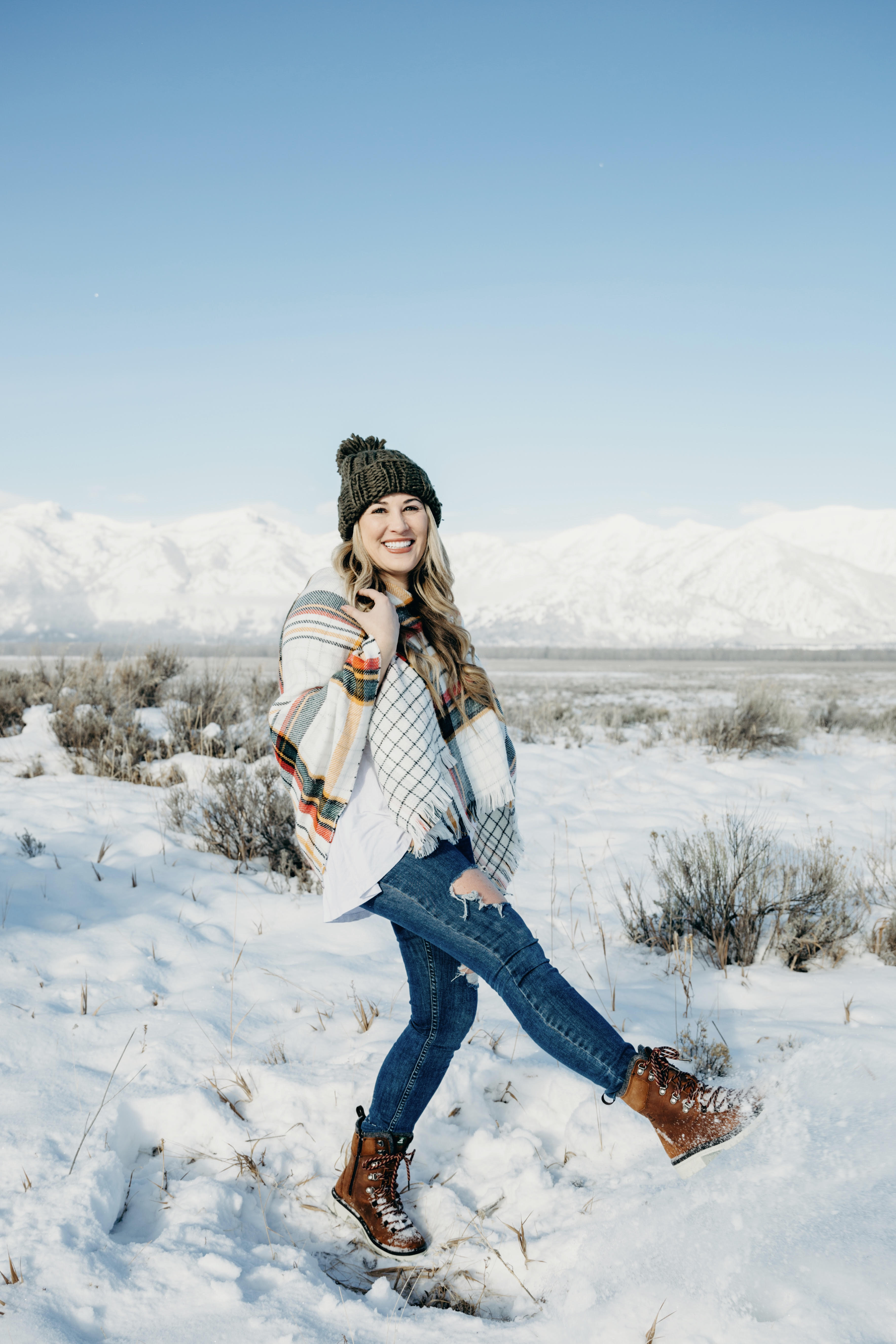 Cold Weather essentials featured by top US fashion blog, Walking in Memphis in High Heels: image of a woman wearing aGrace & Lace plaid poncho, Free People skinny jeans, Grace & Lace pom beanie, and KAMIK hiking boots