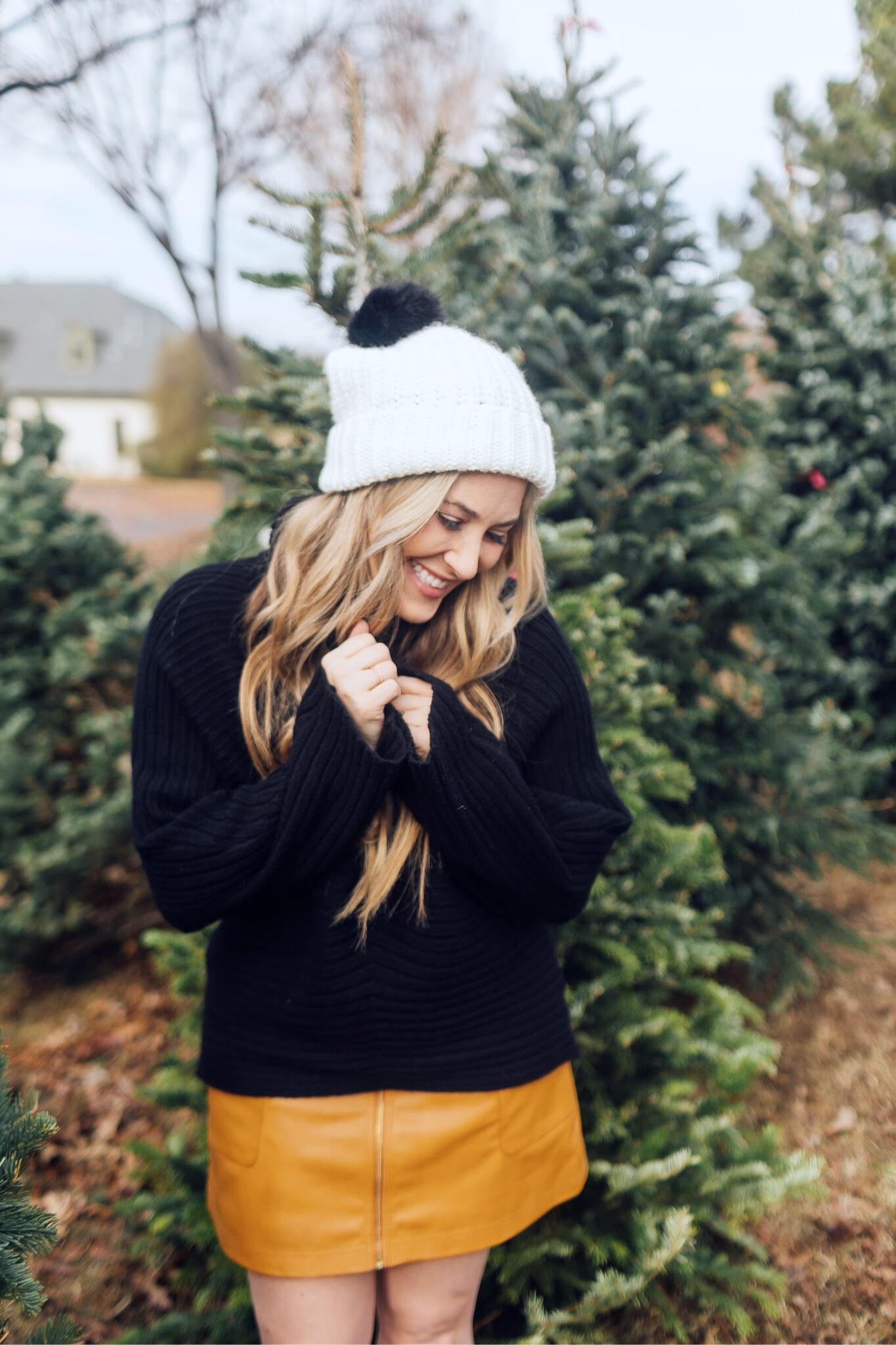 Winter accessories featured by top US fashion blog, Walking in Memphis in High Heels: image of a blonde woman walking in a Christmas tree farm wearing a Free People mini skirt, Melroseand Market sweater, Rebecca Minkoff pompom beanie, Sole Society Sock Bootie