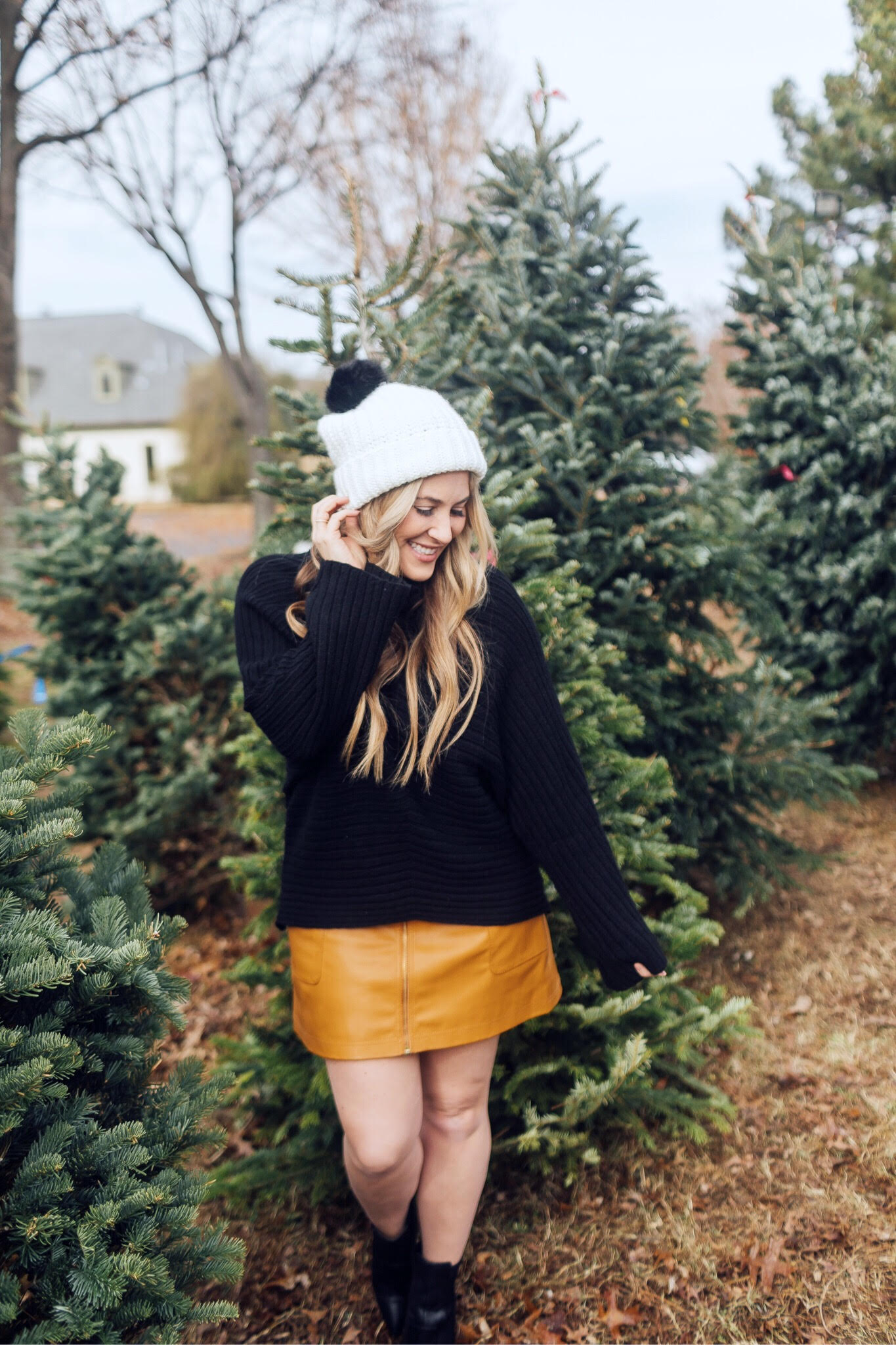 Winter accessories featured by top US fashion blog, Walking in Memphis in High Heels: image of a blonde woman walking in a Christmas tree farm wearing a Free People mini skirt, Melroseand Market sweater, Rebecca Minkoff pompom beanie, Sole Society Sock Bootie