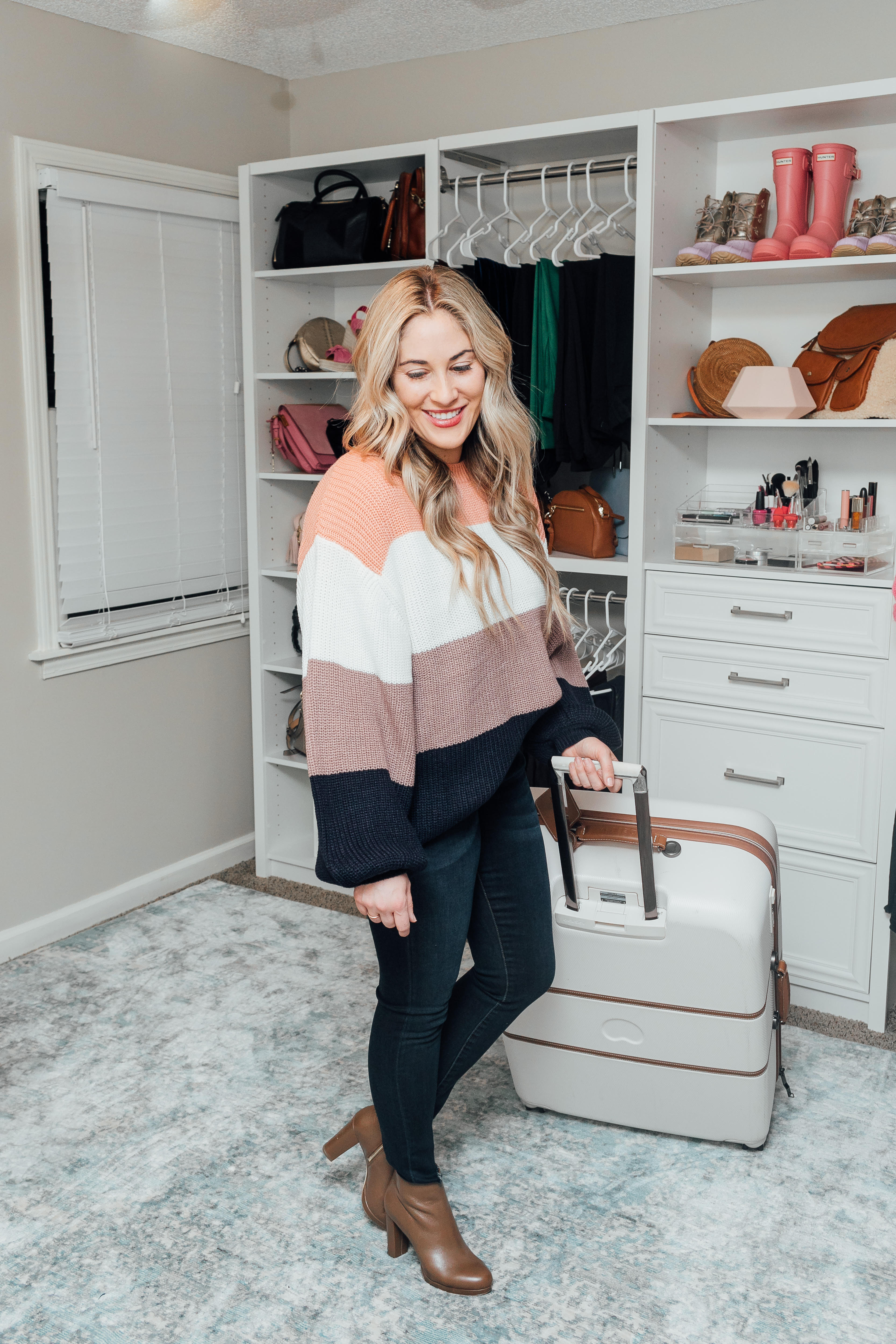 Essentials to pack for your Valentines Getaway: image of a woman wearing a Pink Lily color block sweater, Zappos skinny jeans, and Michael Kors booties and Desley luggage