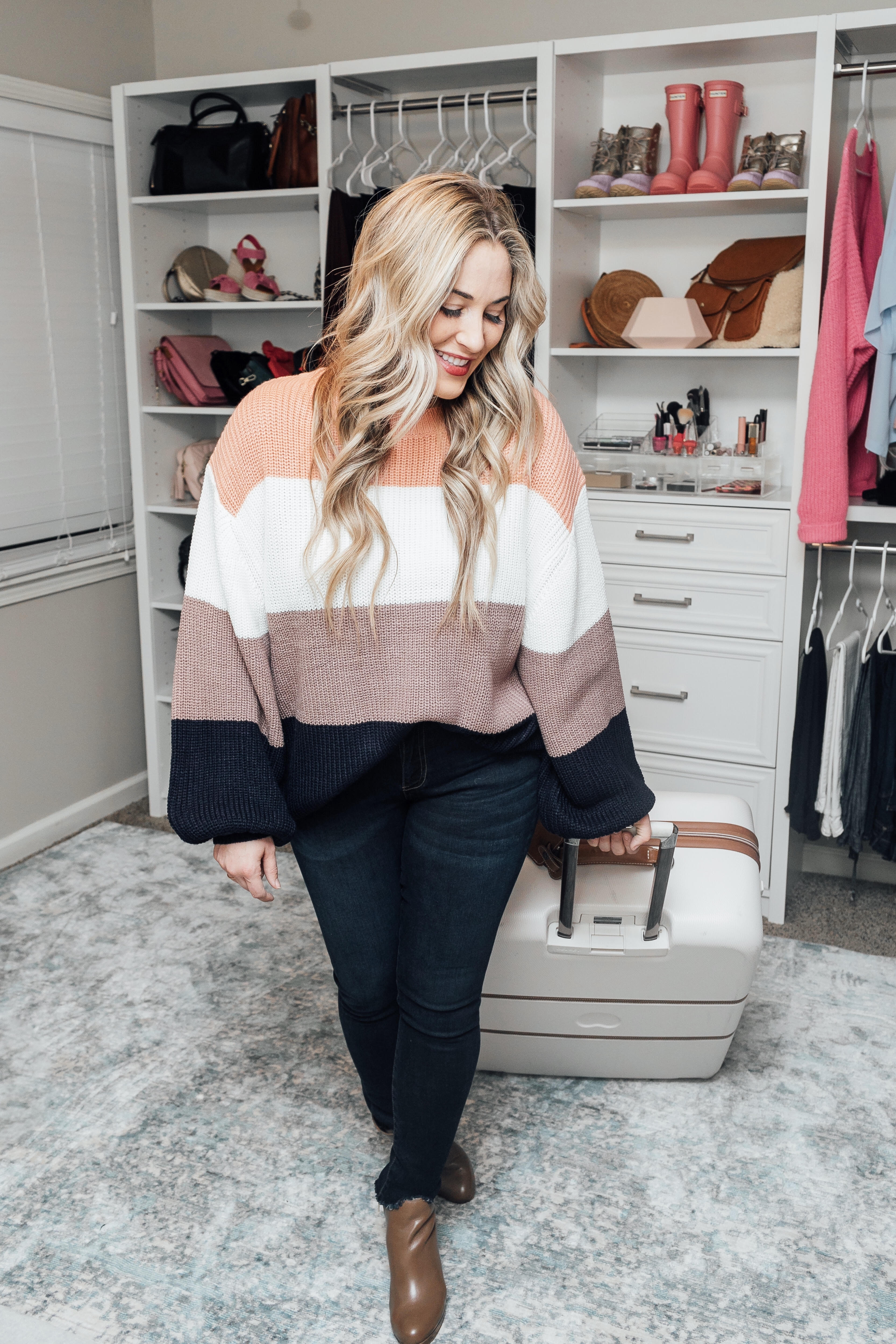 Essentials to pack for your Valentines Getaway: image of a woman wearing a Pink Lily color block sweater, Zappos skinny jeans, and Michael Kors booties and Desley luggage