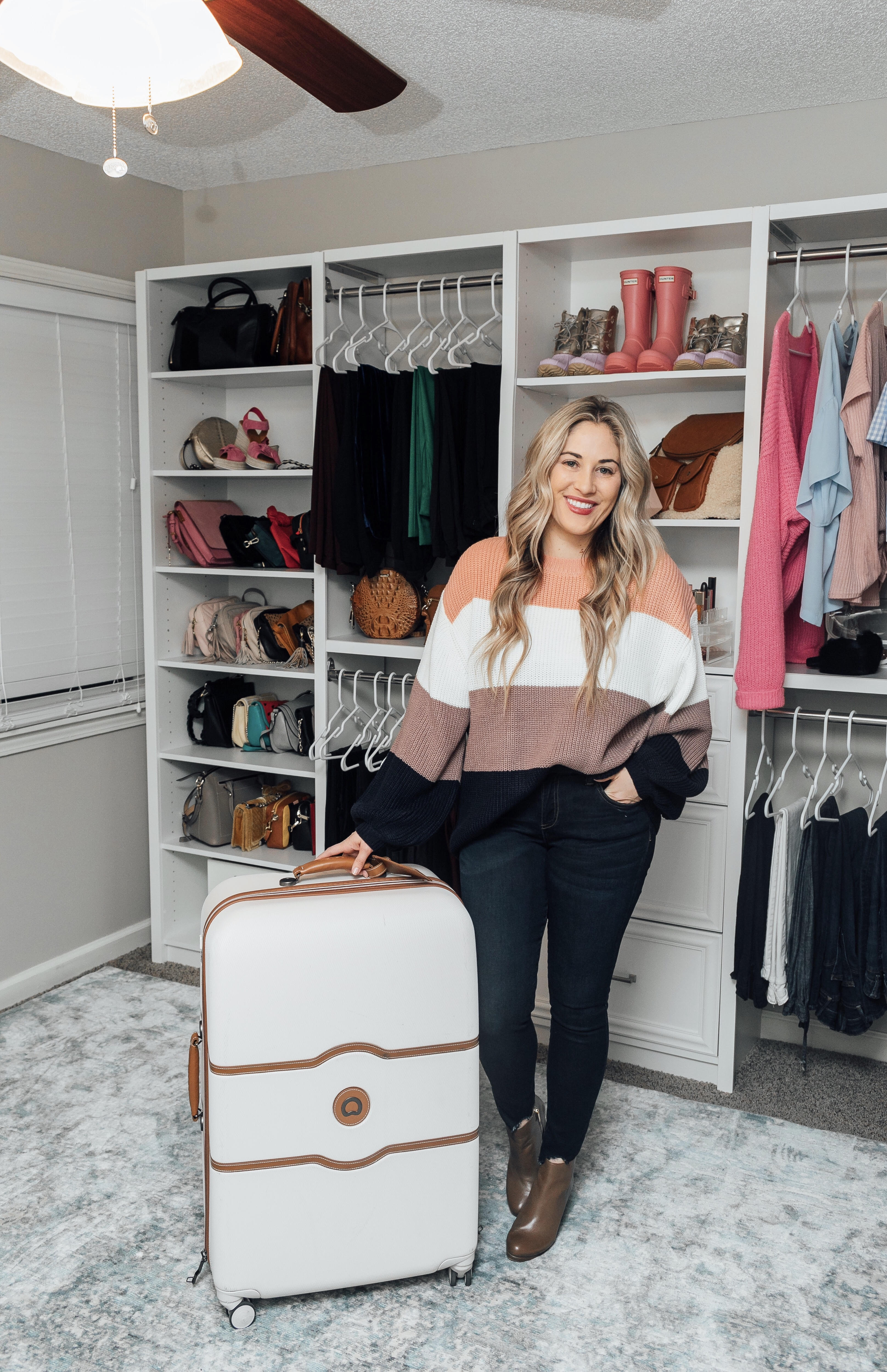 Essentials to pack for your Valentines Getaway: image of a woman wearing a Pink Lily color block sweater, Zappos skinny jeans, and Michael Kors booties and Desley luggage