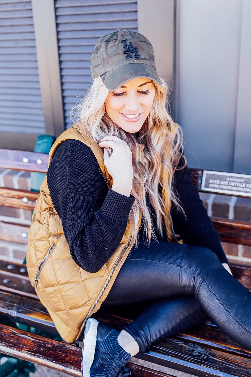 Gold Puffer Vest styled by top US fashion blog, Walking in Memphis in High Heels: image of a woman wearing a Patagonia gold puffer vest, SPANX faux leather leggings, Target tunic sweater, Adidas sneakers, and a LA Dodgers camouflage baseball cap.