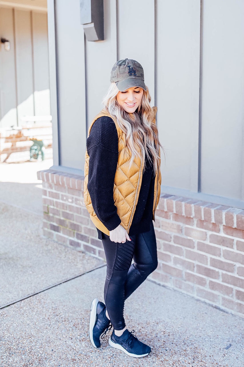 Gold Puffer Vest styled by top US fashion blog, Walking in Memphis in High Heels: image of a woman wearing a Patagonia gold puffer vest, SPANX faux leather leggings, Target tunic sweater, Adidas sneakers, and a LA Dodgers camouflage baseball cap.