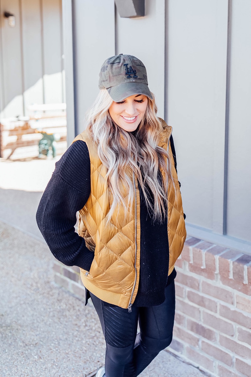 Gold Puffer Vest styled by top US fashion blog, Walking in Memphis in High Heels: image of a woman wearing a Patagonia gold puffer vest, SPANX faux leather leggings, Target tunic sweater, Adidas sneakers, and a LA Dodgers camouflage baseball cap.