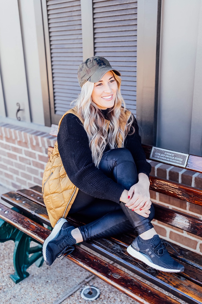 Gold Puffer Vest styled by top US fashion blog, Walking in Memphis in High Heels: image of a woman wearing a Patagonia gold puffer vest, SPANX faux leather leggings, Target tunic sweater, Adidas sneakers, and a LA Dodgers camouflage baseball cap.