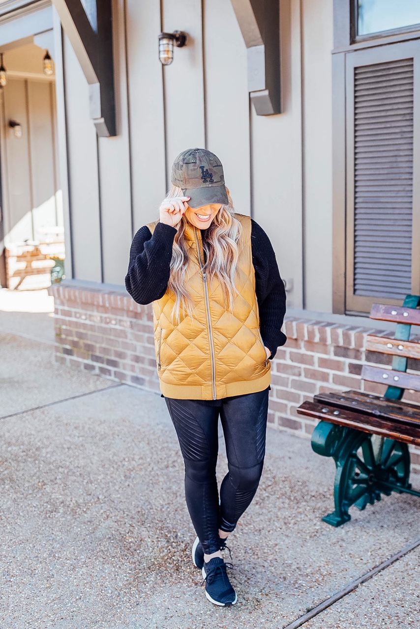 Gold Puffer Vest styled by top US fashion blog, Walking in Memphis in High Heels: image of a woman wearing a Patagonia gold puffer vest, SPANX faux leather leggings, Target tunic sweater, Adidas sneakers, and a LA Dodgers camouflage baseball cap.