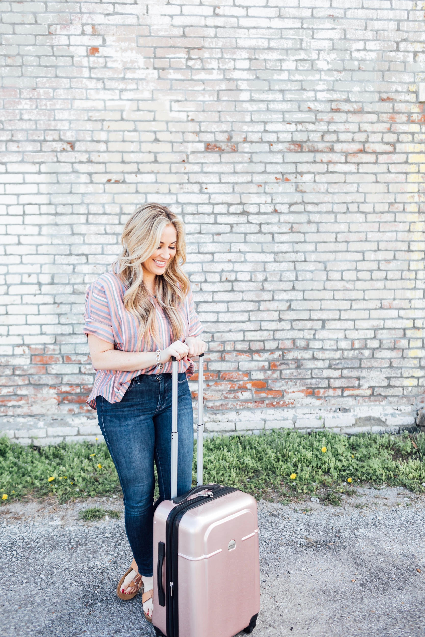 Spring Trip Packing List featured by top US travel and fashion blog, Walking in Memphis in High Heels: image of a woman with a Delsey spinner carry one suitcase