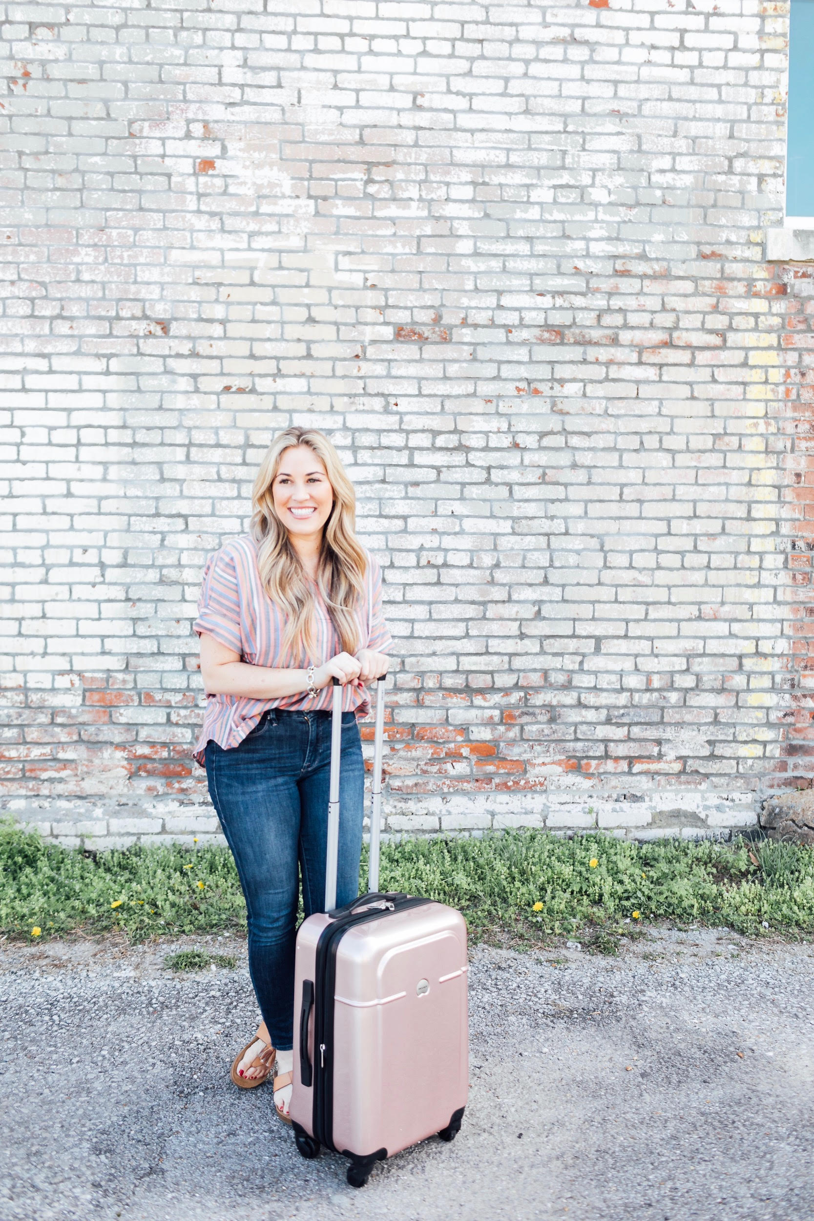 Spring Trip Packing List featured by top US travel and fashion blog, Walking in Memphis in High Heels: image of a woman with a Delsey spinner carry one suitcase