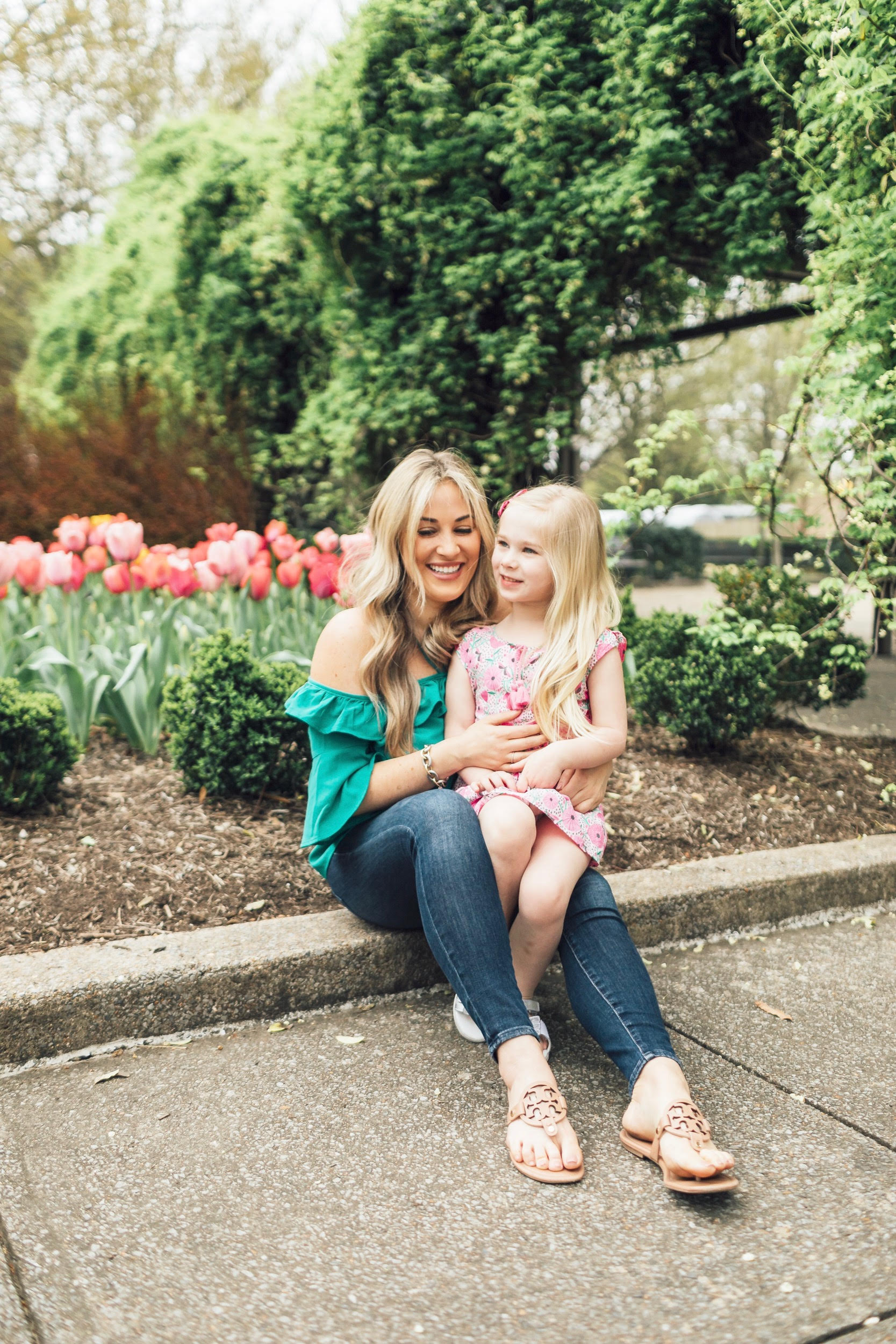 How to Get Cute Family Pictures with Your Child featured by top US life and style blog, Walking in Memphis in High Heels: image of a woman wearing a BB Dakota off the shoulder blouse, Good American skinny jeans, Tory Burch flies flops and her daughter wearing an Egg Baby floral dress and Pediped silver sandals