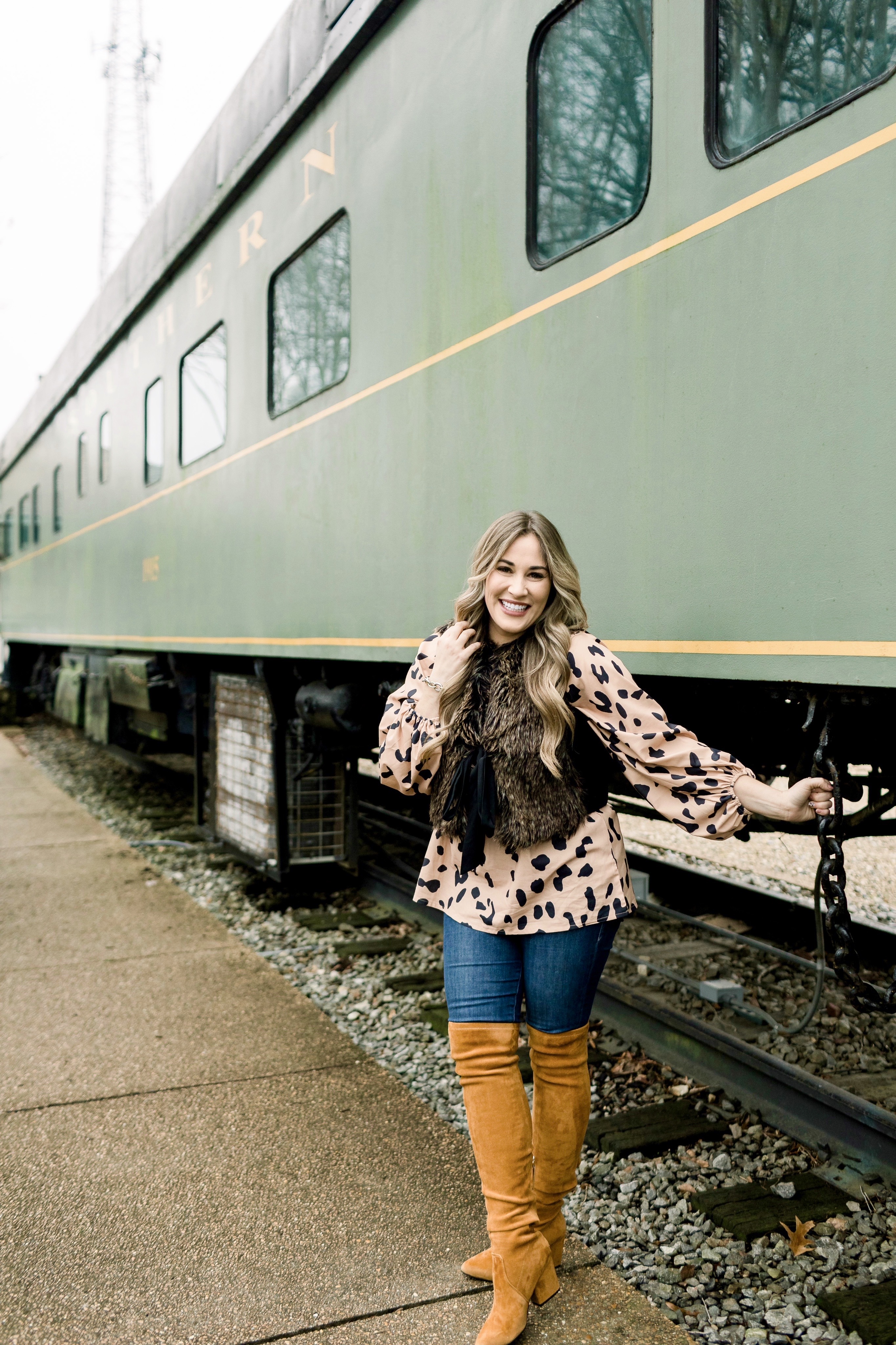 Animal print top styled by top Memphis fashion blog, Walking in Memphis in High Heels: image of a woman wearing an Amazon Chiffon animal print top, LOFT faux fur vest, Good American jeans and Goodnight Macaroon over the knees suede boots.
