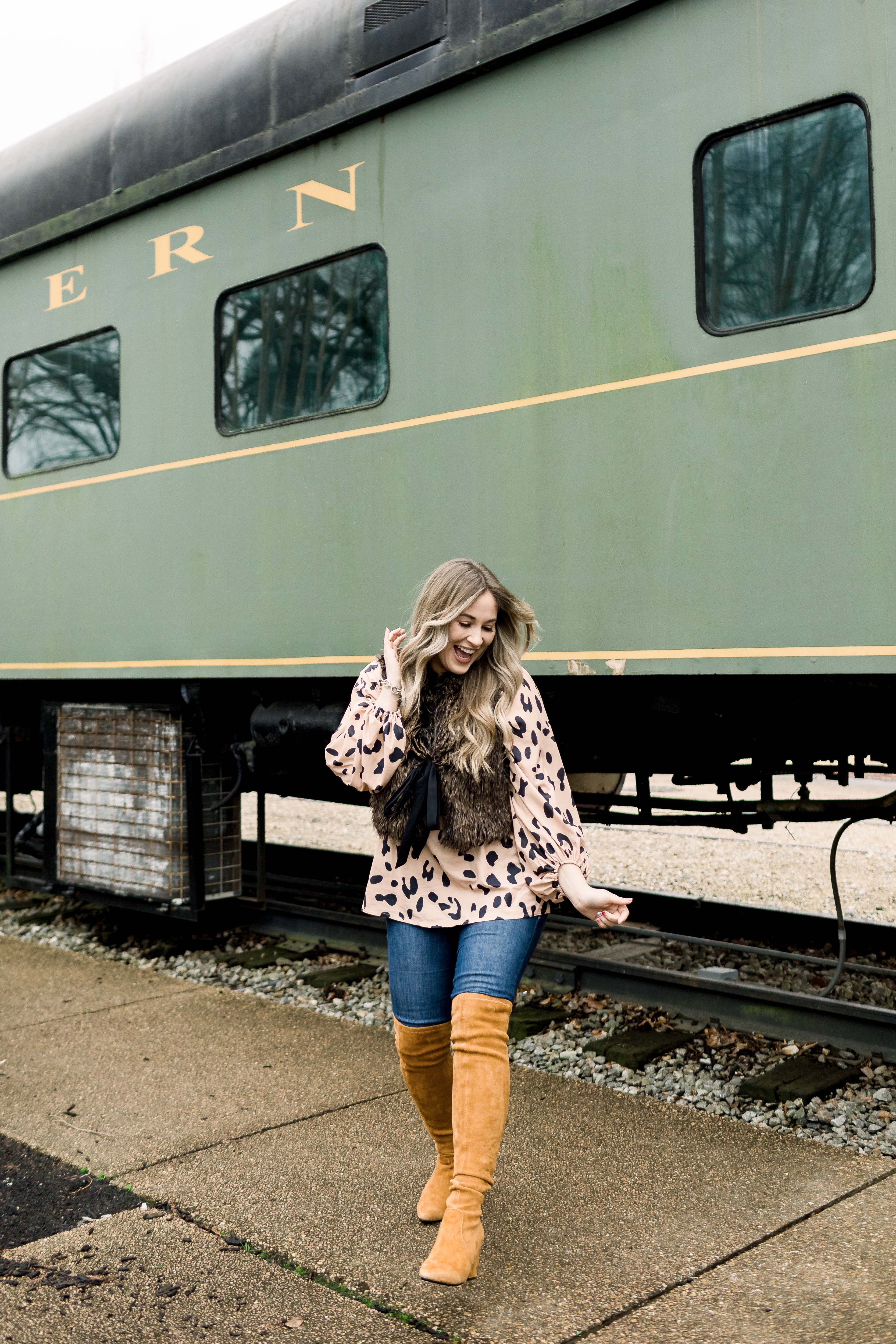 Animal print top styled by top Memphis fashion blog, Walking in Memphis in High Heels: image of a woman wearing an Amazon Chiffon animal print top, LOFT faux fur vest, Good American jeans and Goodnight Macaroon over the knees suede boots.
