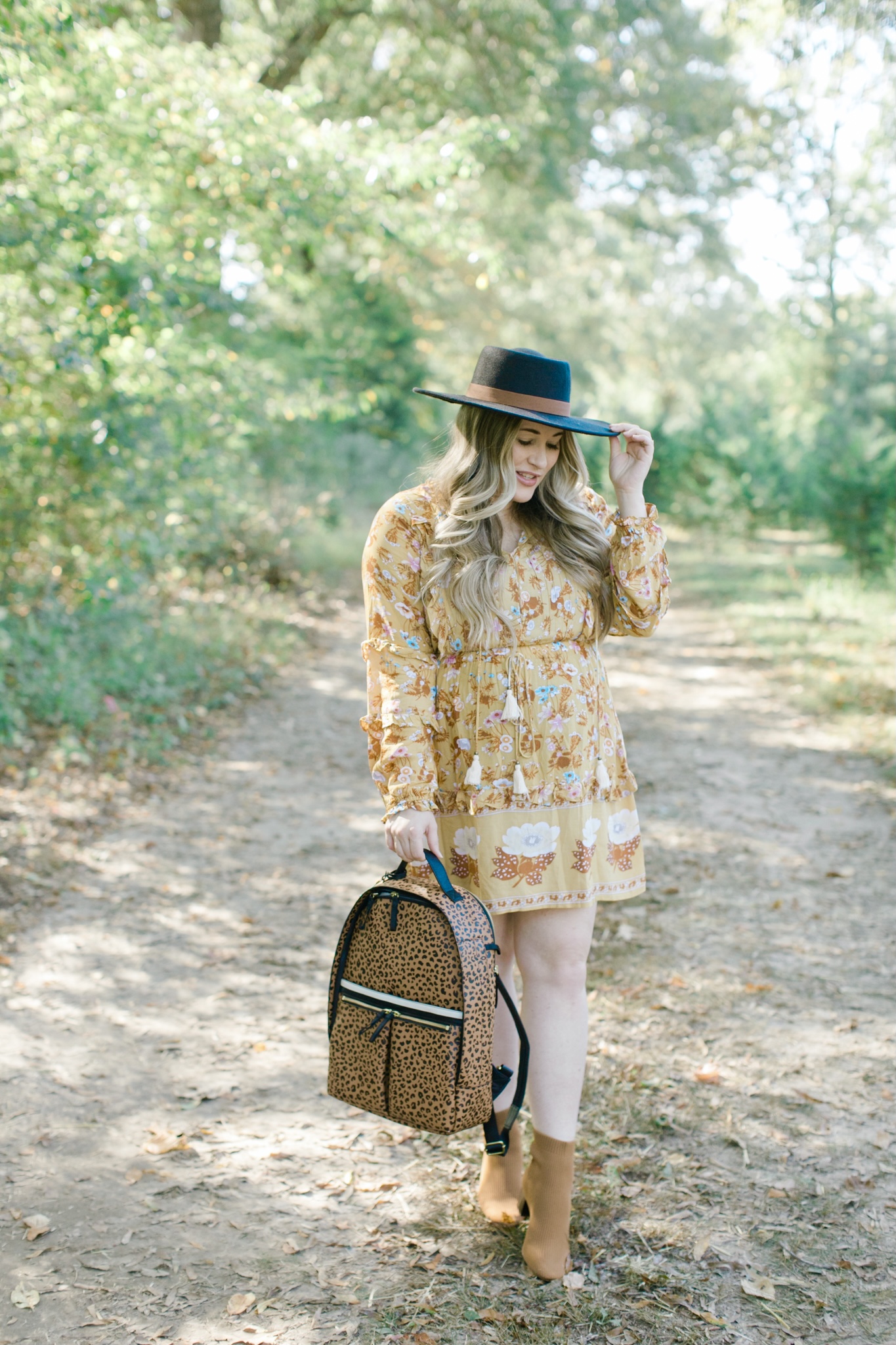 Fall style featured by top Memphis fashion blogger, Walking in Memphis in High Heels: image of a woman wearing a Red Dress floral yellow dress, Everyone booties, and a Fossil backpack.