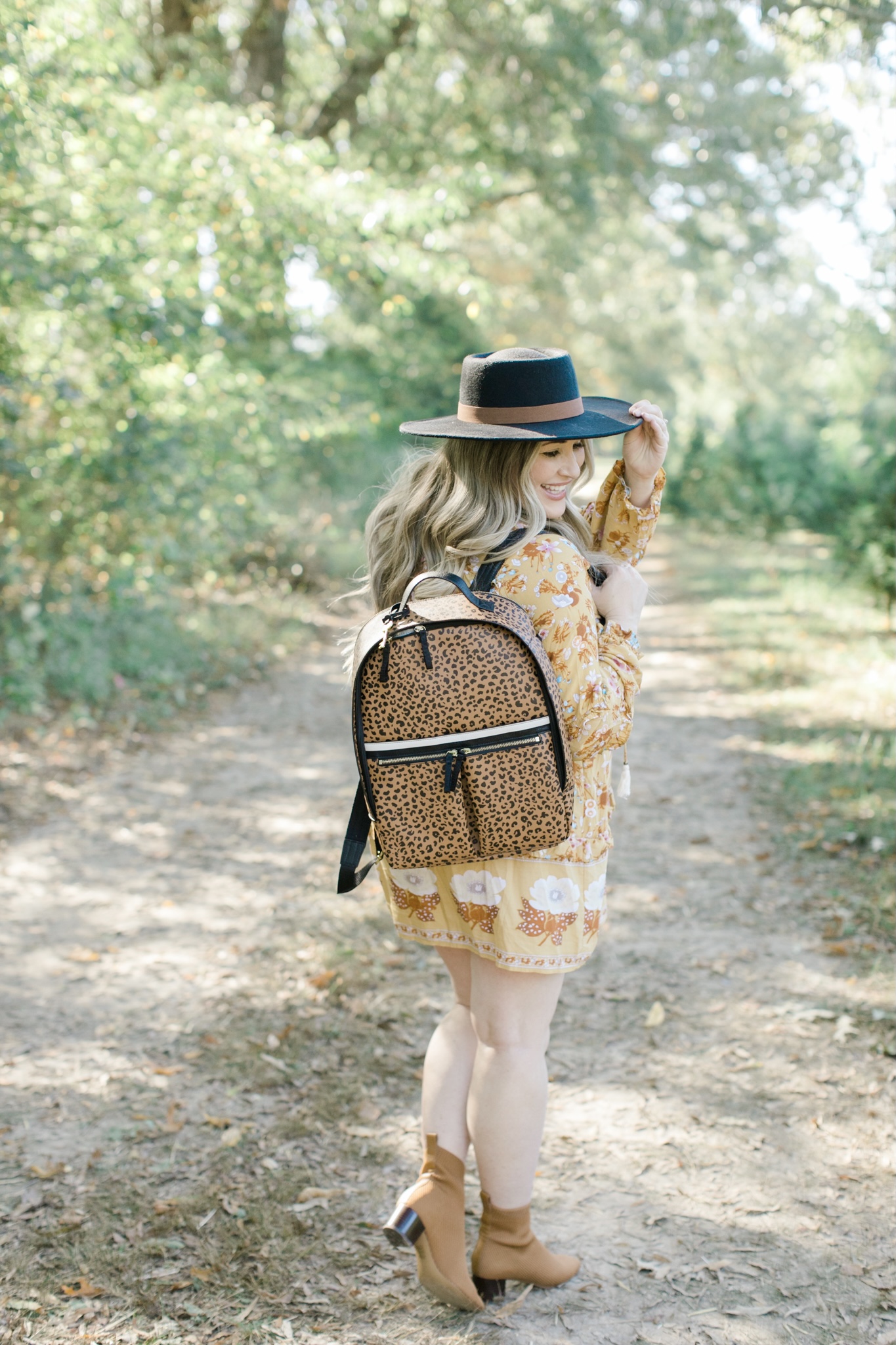 Fall style featured by top Memphis fashion blogger, Walking in Memphis in High Heels: image of a woman wearing a Red Dress floral yellow dress, Everyone booties, and a Fossil backpack.