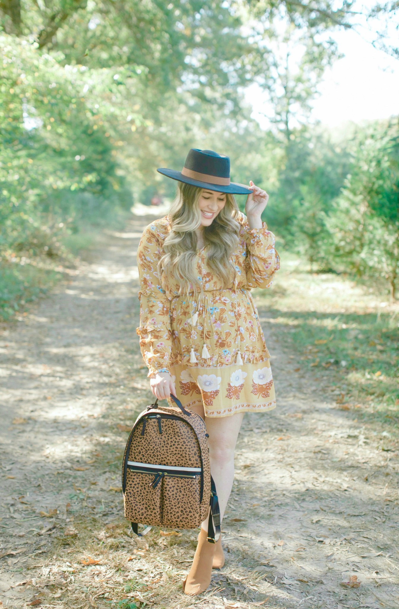 Fall style featured by top Memphis fashion blogger, Walking in Memphis in High Heels: image of a woman wearing a Red Dress floral yellow dress, Everyone booties, and a Fossil backpack.